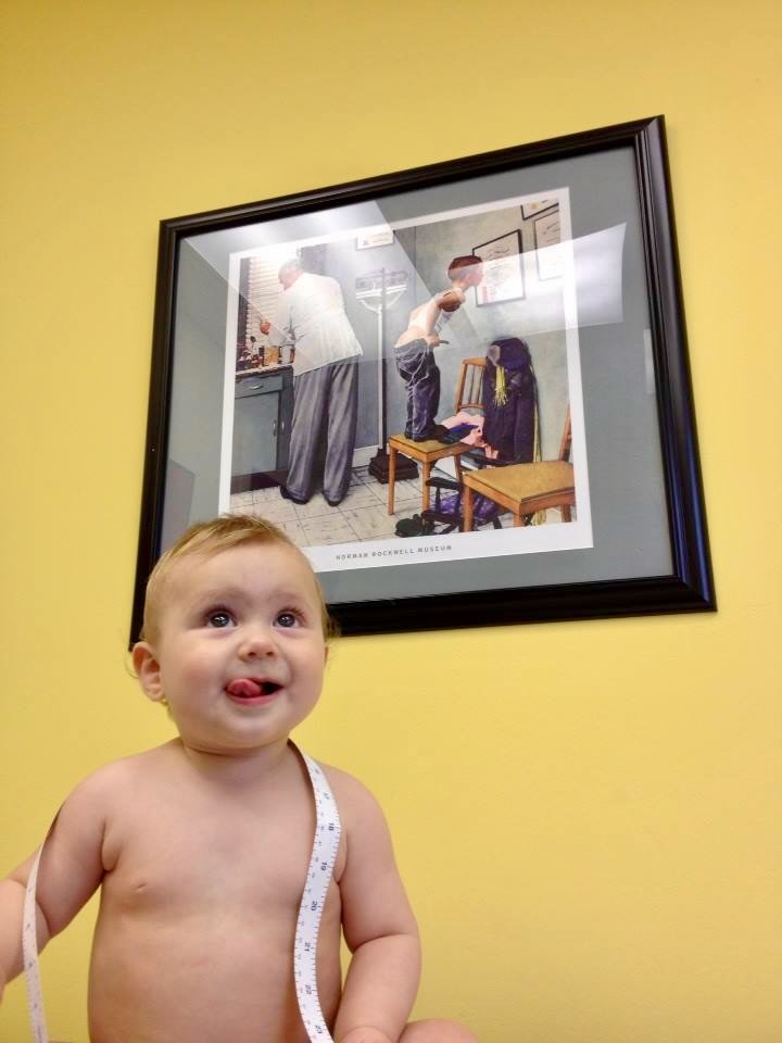 Photo of a baby in a doctor&#39;s office, standing in front of a Norman Rockwell illustration of a doctor&#39;s office.