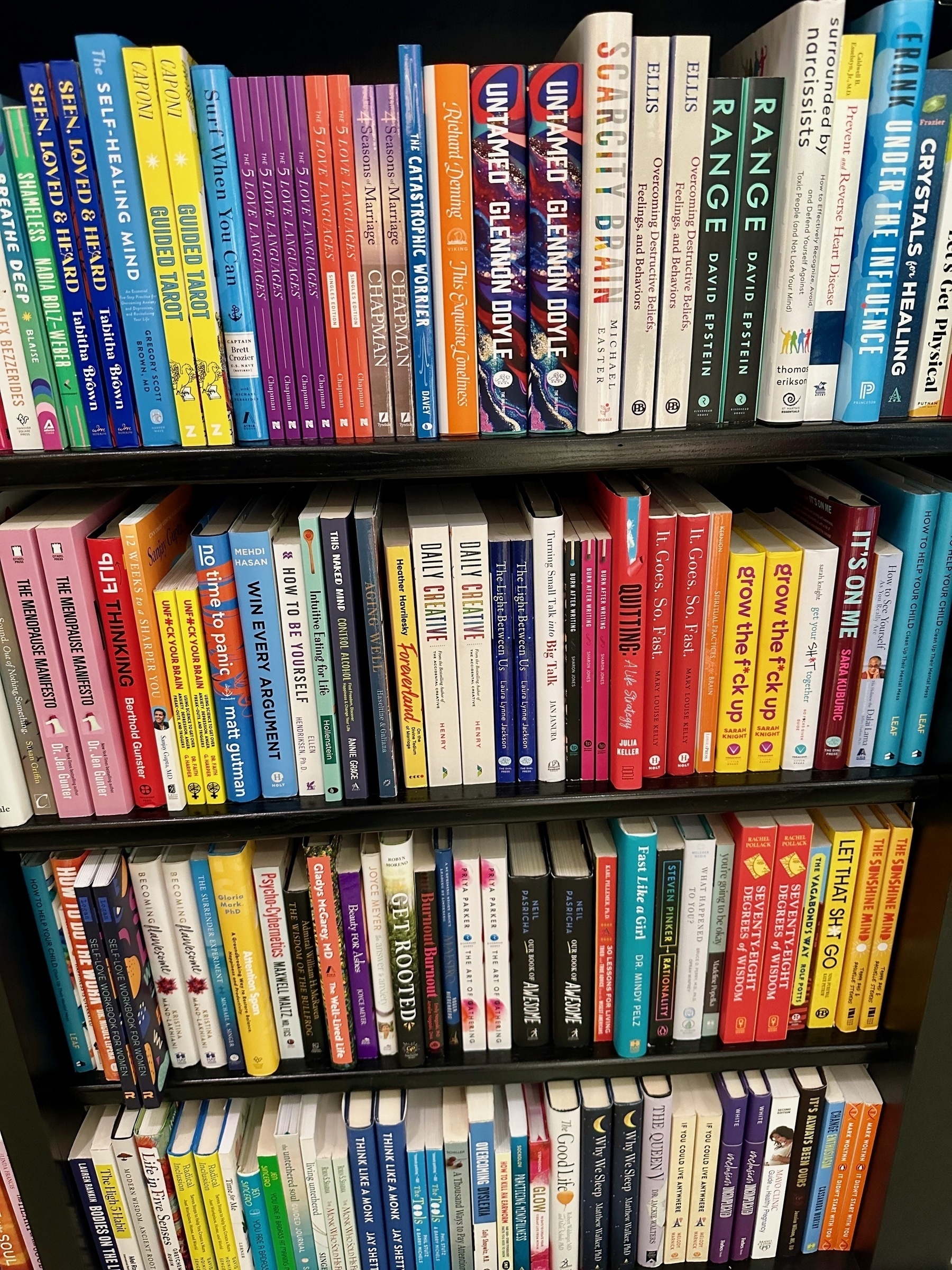 Photo of a bookshelf with dozens of different self-help books lined up.