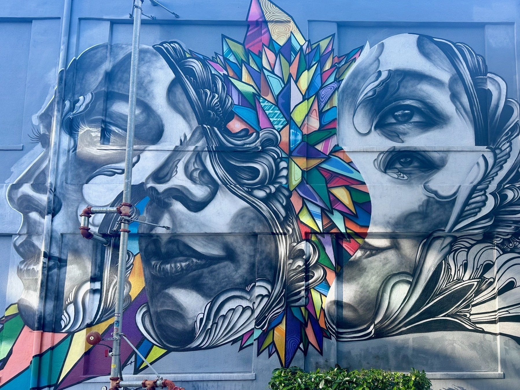 Mural of three broken black and white faces superimposed on one another with colorful fractal crystals shooting out between them.
