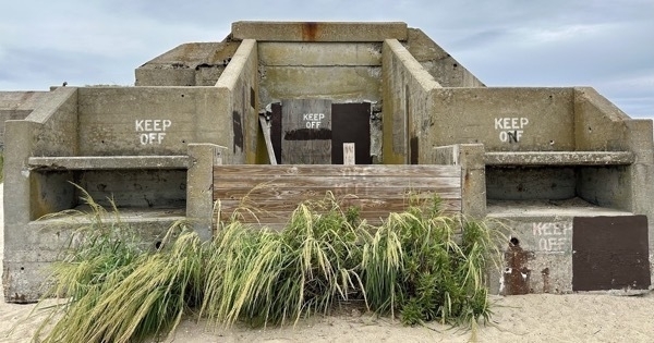 Photo of a concrete bunker with &#39;Keep Off&#39; written on several of the walls. The bunker is on a sandy beach and there is grass growing in front of it.