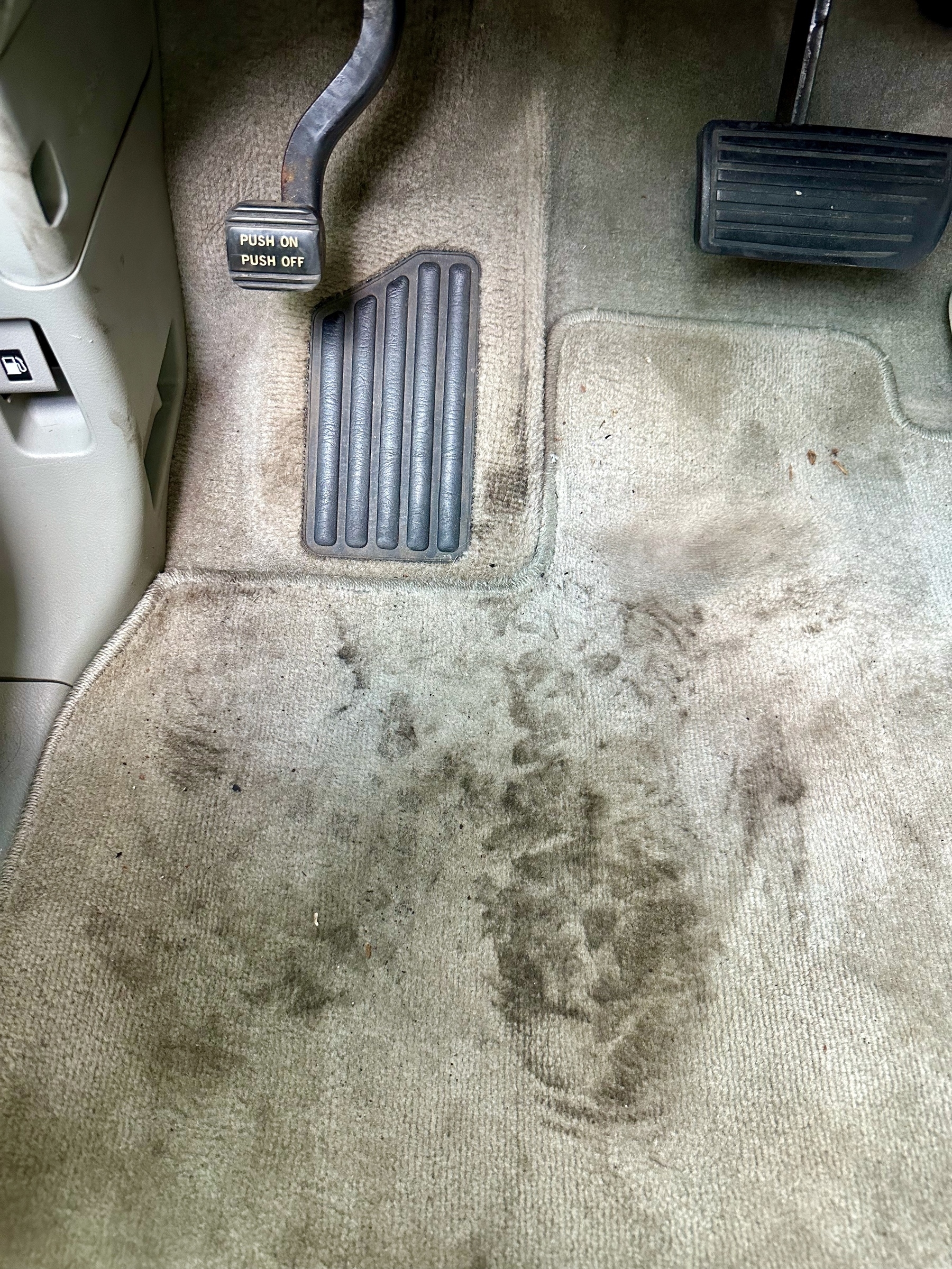 Close-up of a driver&#39;s side car carpet with two large dirty footprints.