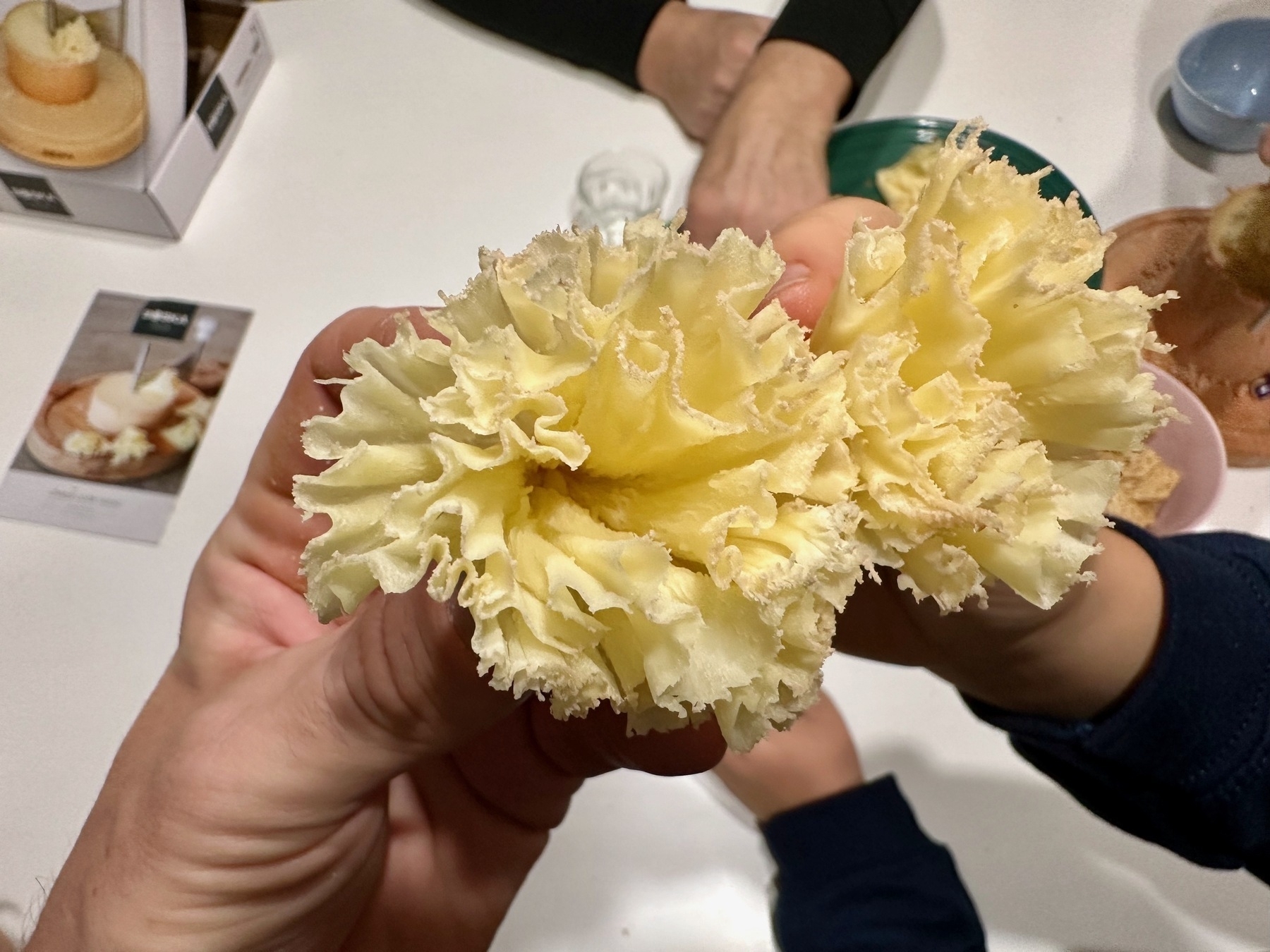 Hands holding cheese cut thinly and folded to resemble a flower. 