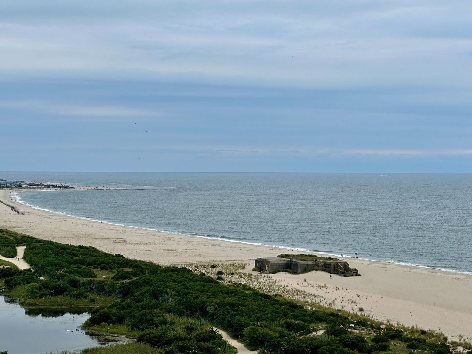 A far-away view of a concrete bunker sitting in the middle of a white sand ocean beach.