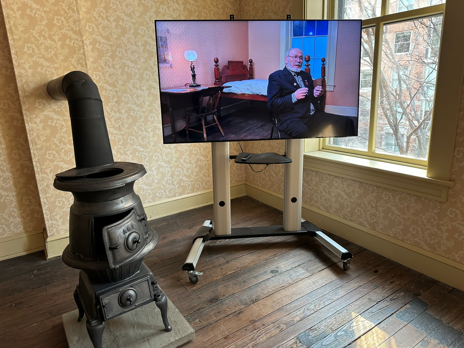 A television set hangs above an iron furnace, showing an elderly man speaking.
